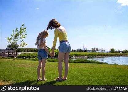summer and vacation, girls sisters on the meadow near the river