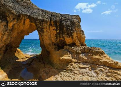 Summer Atlantic rocky coast view with natural arch and splashes (Albufeira outskirts, Algarve, Portugal).