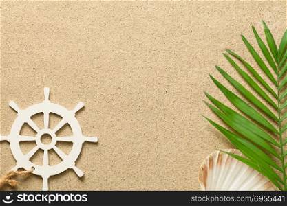 Summer background with green palm leaf, decorative ship steering wheel and shell. Beach texture. Copy space. Top view