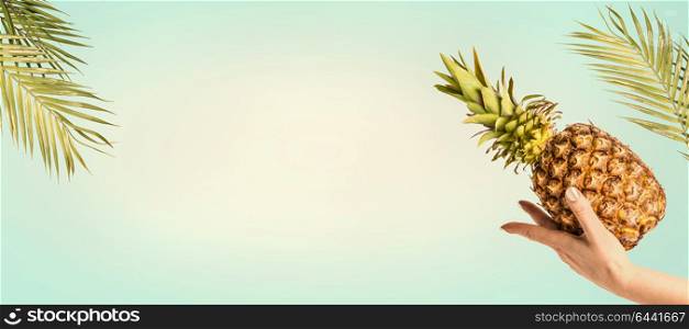 Summer background with palm leaves, female hand with pineapple at sunny sky background, banner or template with copy space for your design