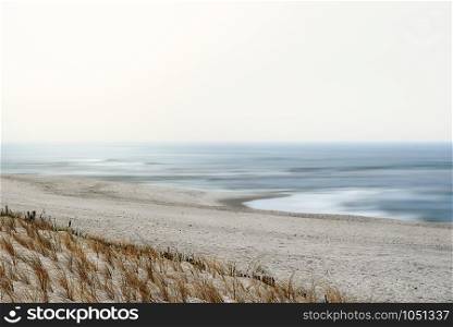 Summer beach landscape with the north sea blue water, white sands and European beachgrass, the Ammophila, under overcast sky, on Sylt island, Germany.