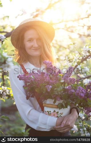 summer - beautiful girl in hat and suspenders at the garden with a bouquet of lilacs