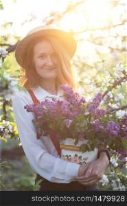 summer - beautiful girl in hat and suspenders at the garden with a bouquet of lilacs