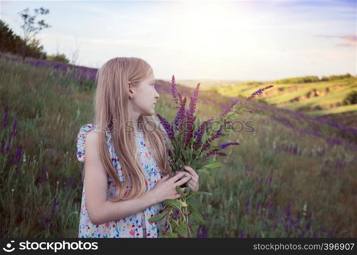 summer - beautiful girl on a meadow with a bouquet of salvia