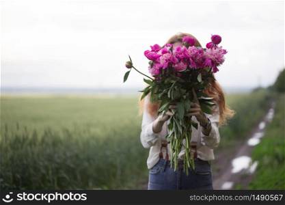 summer - Beautiful girl with a bouquet peony covers his face at the field