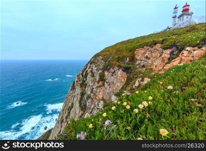 Summer blossoming Cape Roca (Cabo da Roca) with flowers and lighthouse. Atlantic ocean coast view in cloudy weather, Portugal.