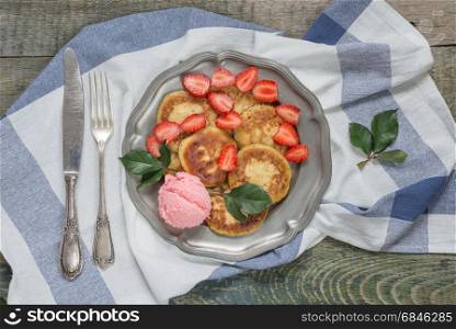 Summer breakfast of pancakes with ice cream and ripe berries of strawberry on an antique tin plate, with vintage knife and fork, top view
