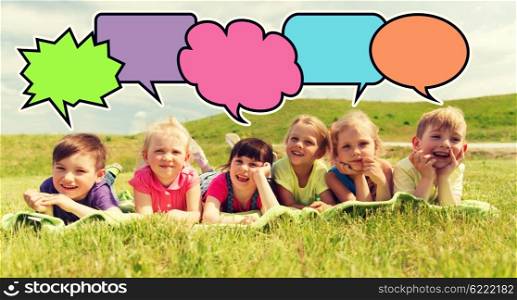 summer, childhood, leisure and people concept - group of happy kids lying on blanket or cover outdoors with colorful text bubble icons