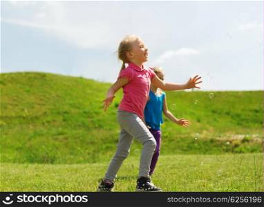 summer, childhood, leisure and people concept - group of happy kids playing tag game and running on green field outdoors