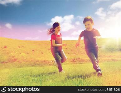 summer, childhood, leisure and people concept - happy little boy and girl playing tag game and running outdoors on green field. happy little boy and girl running outdoors