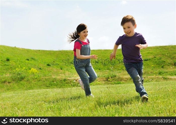 summer, childhood, leisure and people concept - happy little boy and girl playing tag game and running outdoors on green field