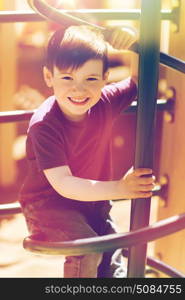 summer, childhood, leisure and people concept - happy little boy on children playground climbing frame. happy little boy climbing on children playground. happy little boy climbing on children playground