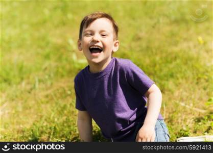 summer, childhood, leisure and people concept - happy little boy sitting on grass and laughing outdoors