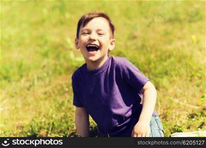 summer, childhood, leisure and people concept - happy little boy sitting on grass and laughing outdoors