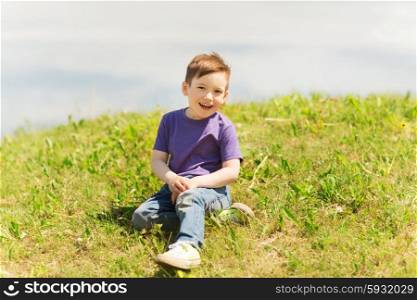 summer, childhood, leisure and people concept - happy little boy sitting on grass outdoors