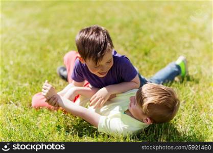 summer, childhood, leisure and people concept - happy little boys outdoors fighting for fun on green field