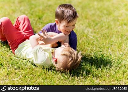 summer, childhood, leisure and people concept - happy little boys outdoors fighting for fun on green field