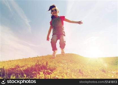 summer, childhood, leisure and people concept - happy little girl jumping high over green field and blue sky outdoors. happy little girl jumping high outdoors