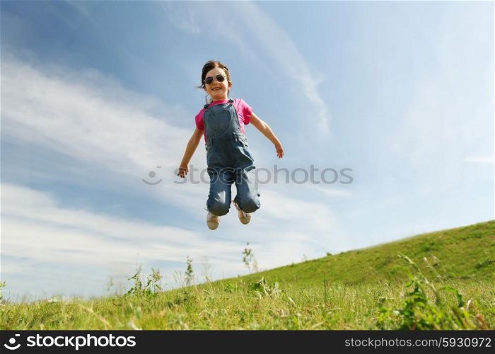 summer, childhood, leisure and people concept - happy little girl jumping high over green field and blue sky outdoors