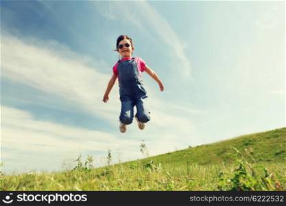 summer, childhood, leisure and people concept - happy little girl jumping high over green field and blue sky outdoors