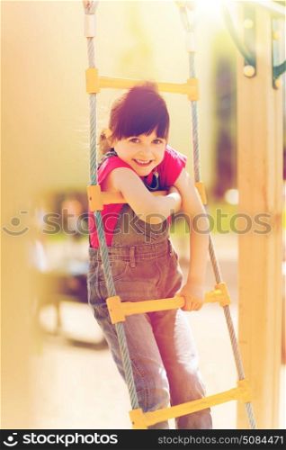 summer, childhood, leisure and people concept - happy little girl on children playground climbing by rope-ladder. happy little girl climbing on children playground. happy little girl climbing on children playground