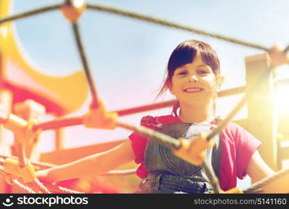 summer, childhood, leisure and people concept - happy little girl on children playground climbing frame. happy little girl climbing on children playground