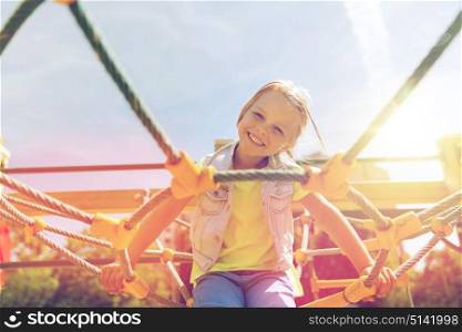 summer, childhood, leisure and people concept - happy little girl on children playground climbing frame. happy little girl climbing on children playground