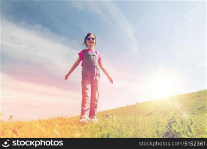 summer, childhood, leisure and people concept - happy little girl over green field and blue sky outdoors. happy little girl over green field and blue sky