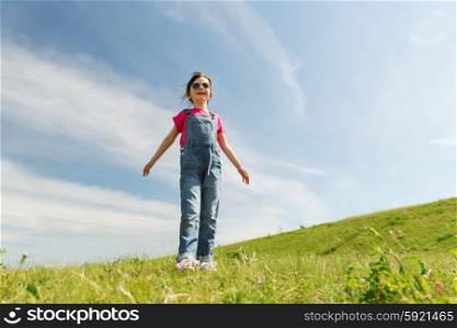 summer, childhood, leisure and people concept - happy little girl over green field and blue sky outdoors