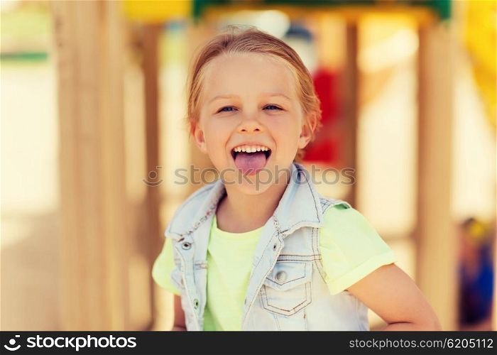summer, childhood, leisure and people concept - happy little girl showing tongue and having fun on playground
