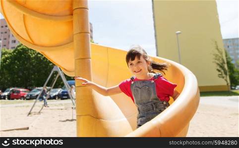 summer, childhood, leisure and people concept - happy little girl sliding on slide at children playground