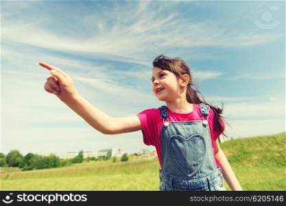 summer, childhood, leisure, direction and people concept - happy little girl pointing finger on green summer field