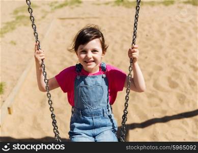 summer, childhood, leisure, friendship and people concept - happy little girl swinging on swing at children playground