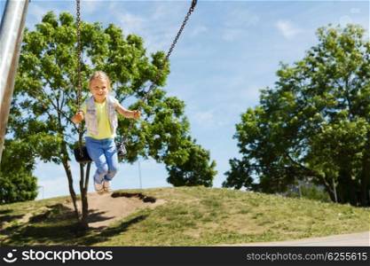 summer, childhood, leisure, friendship and people concept - happy little girl swinging on swing at children playground