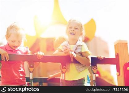 summer, childhood, leisure, friendship and people concept - happy little girls laughing on children playground climbing frame. happy little girls on children playground