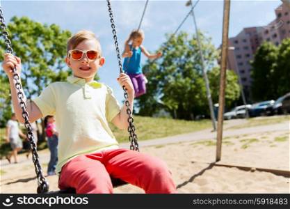 summer, childhood, leisure, friendship and people concept - two happy kids swinging on swing at children playground