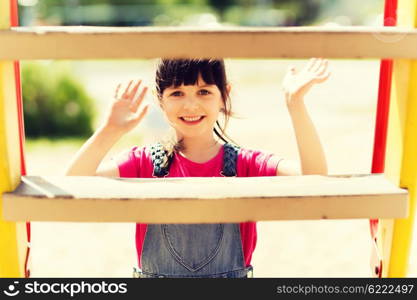 summer, childhood, leisure, gesture and people concept - happy little girl waving hand on children playground climbing frame