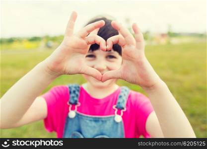 summer, childhood, leisure, love and people concept - happy little girl making heart shape gesture on green summer field