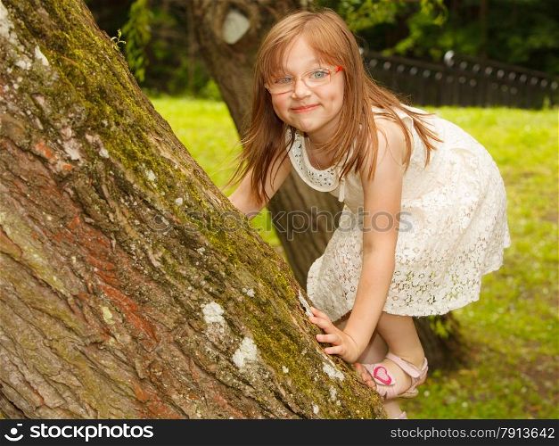 Summer children and happy chilghood concept. little girl having fun playing climbing to tree in park outdoors.