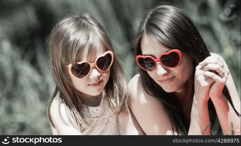 Summer children and happy family concept. Mother and daughter little girl in heart shaped sunglasses, having picnic playing in park outdoors.