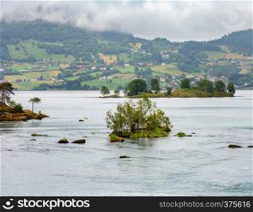 Summer cloudy fjord landscape with fir forest and settlement on shore, Norway.
