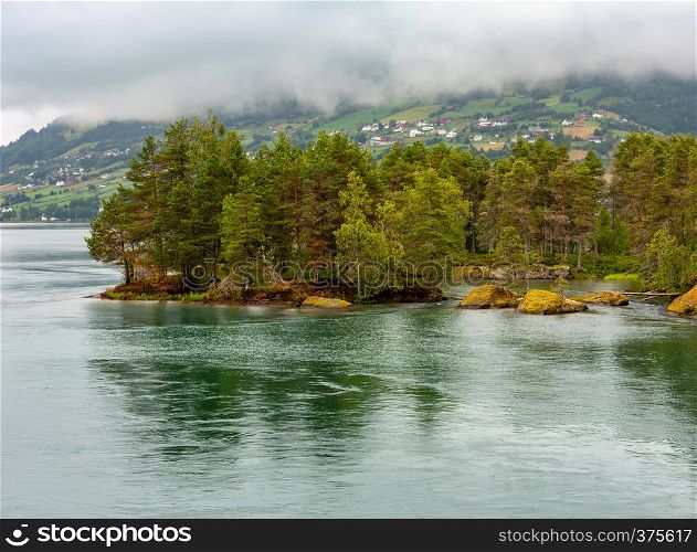 Summer cloudy fjord landscape with fir forest on stony shore, Norway