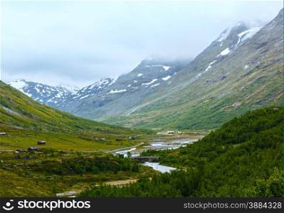 Summer cloudy mountain landscape with river and rural houses (Norway).