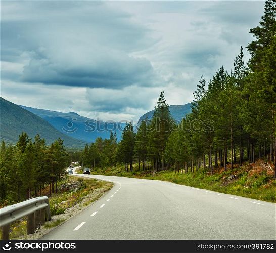 Summer cloudy mountain landscape with serpentine secondary road, Norway. Car models unrecognizable.
