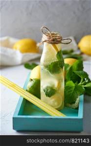summer cold drink with lemons, mint leaves, lime in a glass bottle, near the ingredients for making lemonade