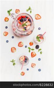 Summer drink with berries and ice cubes. Jug or Pitcher with berries lemonade,Glasses , straw and ingredients on white wooden background, top view. Healthy vitamin drink.