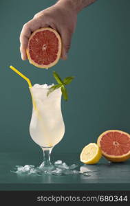 Summer drink with ice cubes, peppermint leaves and citrus fruits aroma. Grapefruits and lemons cold beverage in a glass against a blue background