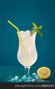 Summer drink with lemons, ice cubes and peppermint on a blue table. Refreshing lemon drink in a frosty glass