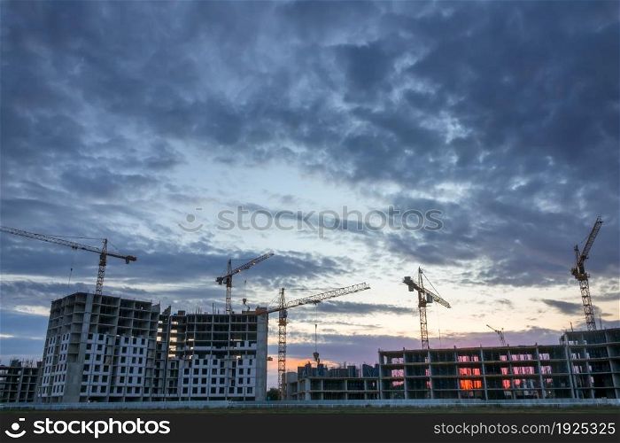 Summer dusk at the construction of residential buildings. Lots of cranes are in operation. Construction Cranes and Dusk Clouds