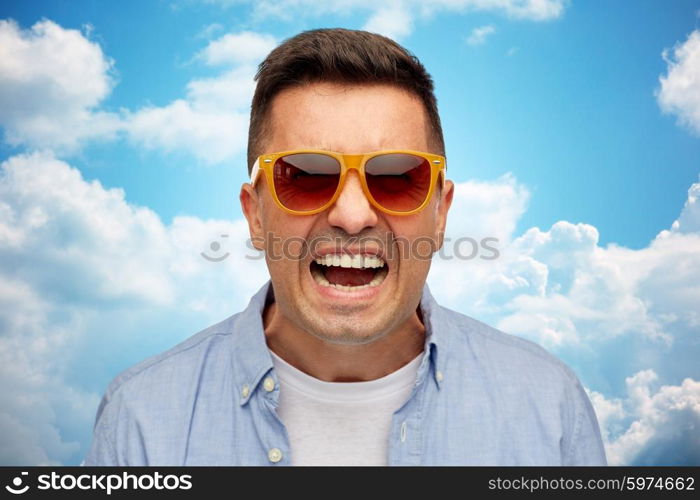 summer, emotions , style and people concept - face of angry middle aged latin man in shirt and sunglasses over blue sky and clouds background